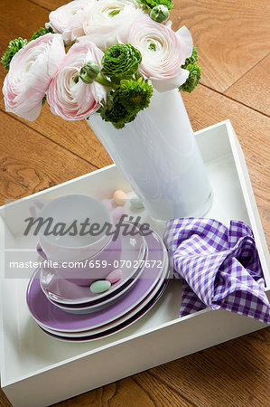 A bunch of spring flowers in a vase alongside a stack of side plates and coffee cups