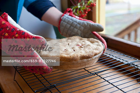 A Person Wearing Oven Mitts Placing a Fresh Baked Cherry Pie on Cooling Racks Near a Window