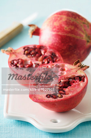 A whole and a halved pomegranate on a chopping board with a knife A whole and a halved pomegranate on a chopping board with a knife