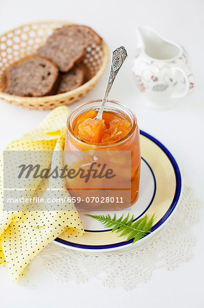 An Open Jar of Melon Jam with a Spoon; Basket of Bread