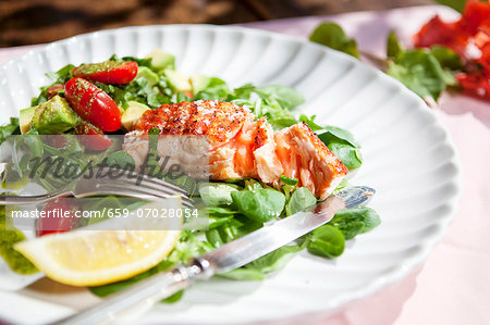 A salmon fillet on a bed of lamb's lettuce with tomatoes, avocado and pesto