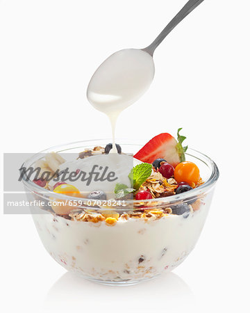 Yoghurt being spooned over a bowl of fruit muesli