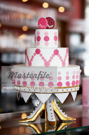An unconventional wedding cake decorated with pink buttons on a gilded cake stand