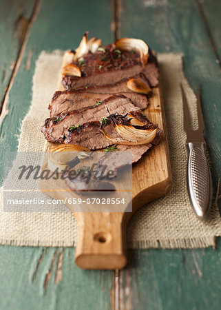 Sliced Flank Steak with Onions and Mushrooms on a Cutting Board