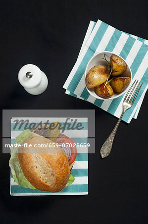 A hamburger with lettuce, tomato and gherkin, served with rosemary potatoes