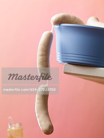 Raw white sausages hanging over the edge of a blue plastic bowl