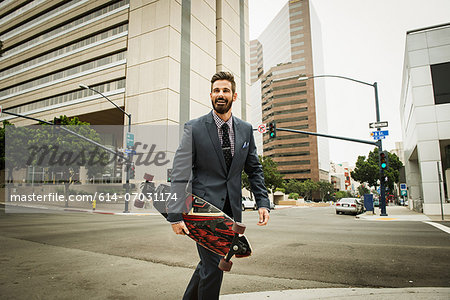 Young businessman carrying skateboard and crossing street