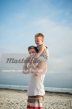 Young man carrying son on shoulders on beach