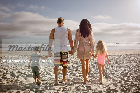 Young family holding hands together on beach, rear view