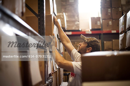 Worker reaching up for cardboard box stored in warehouse