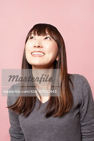 Mid adult woman smiling and looking up against pink background