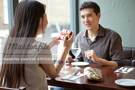 Young couple in restaurant, woman holding gift box