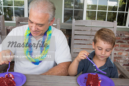 Grandson and senior man eating birthday cake