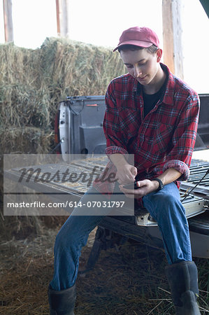 Young farmer sitting and using mobile phone