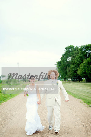 Portrait of couple on wedding day running on dirt track