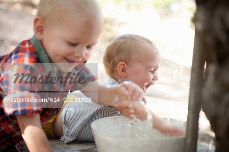 Toddler twins splashing in bowl of water