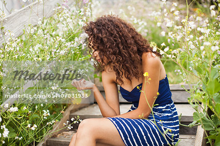 Young woman sitting on wooden steps looking at flower