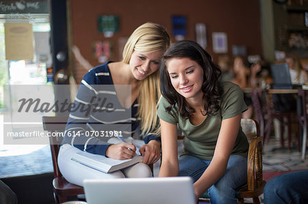 Two teenage girls using textbooks and computer in cafe