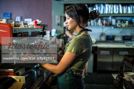 Teenage waitress preparing coffee in cafe kitchen