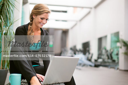 Young woman in gym corridor using laptop