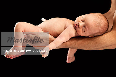 Newborn boy lying on his dad's arms over black background