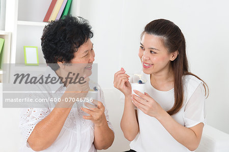 Eating yoghurt . Happy Asian family eating yogurt at home. Beautiful senior mother and adult daughter, healthcare concept.