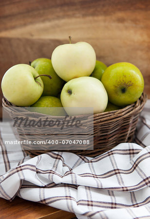 Fresh green and yellow apples in basket on wooden table and wooden background