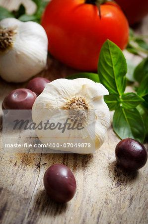 Food ingredinets. Garlic, olives, tomato and basil on wooden table.