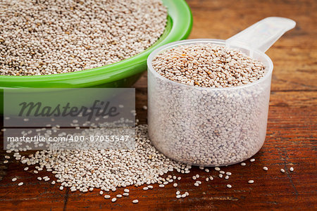 white chia seeds -measuring scoop and small side dish bowl against grunge wooden surface