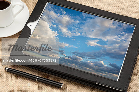 cloud computing concept - a stormy cloudscape on digital tablet computer together with a cup of coffee and stylus pen