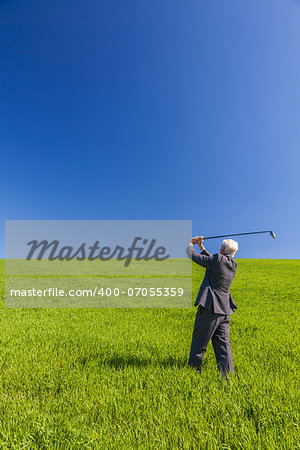 Business concept shot showing an old male man businessman playing golf in a green field with a blue sky.