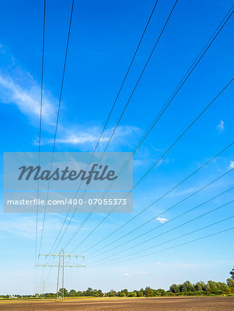 Power cable and power pole in a field under a blue sky with white clouds