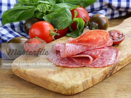 smoked sausage, tomatoes and basil on a wooden cutting board