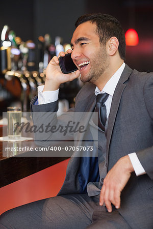 Cheerful businessman on the phone having a drink in a classy bar