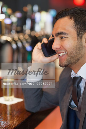 Smiling businessman on the phone having a drink in a classy bar