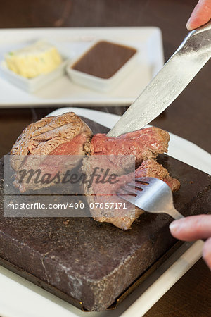 Medium rare steak sizzling on hot stone plate being sliced served in classy restaurant