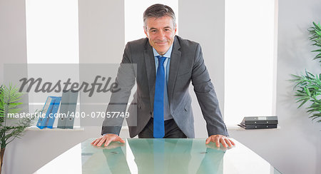 Happy mature businessman standing firmly in front of a desk at office