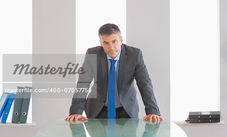 Frowning mature businessman standing firmly in front of a desk at office