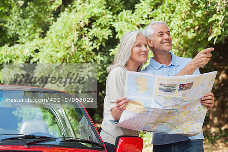 Cheerful mature couple by their cabriolet reading map looking for direction