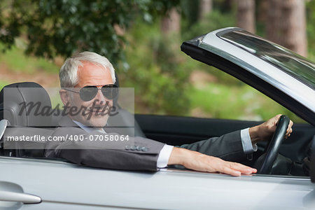 Smiling mature businessman driving classy cabriolet on sunny day