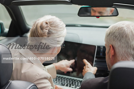 Business people working together on laptop in classy cabriolet on a bright day