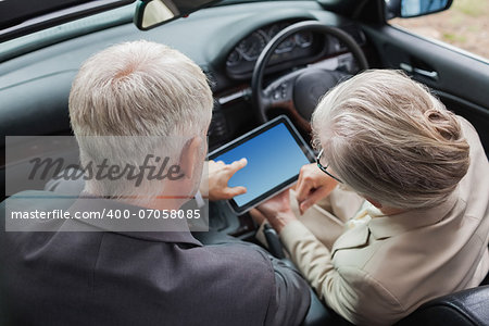 Mature partners working together on tablet in classy car on a bright day