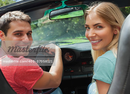 Cheerful couple looking at camera over shoulder while having a ride in cabriolet