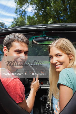 Smiling couple looking over shoulder at camera while having a ride in cabriolet