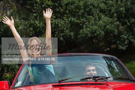 Happy woman having fun in red classy cabriolet while her boyfriend driving