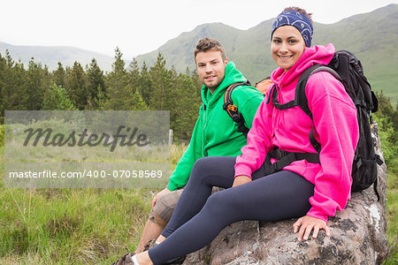 Couple sitting on a rock resting during hike smiling at camera