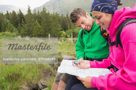 Couple sitting on a rock resting during hike using map and compass in the countryside