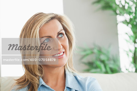 Thinking blonde woman sitting on a sofa in a living room