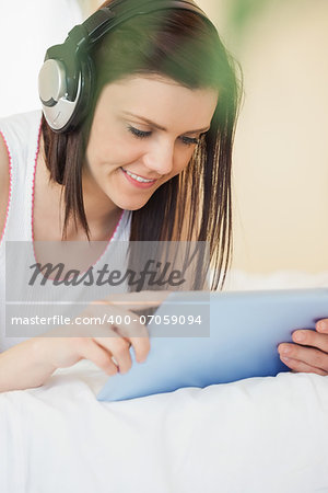 Happy girl listening to music with a headset and using a tablet pc lying on a bed in a bedroom