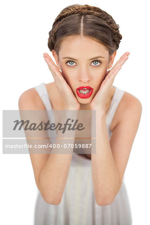 Shocked model in white dress posing holding her head on white background